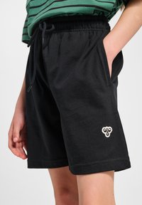 Svarta bomullsshorts med elastisk midja och dragsko. Har sidfickor och en liten broderad design på nedre benet.