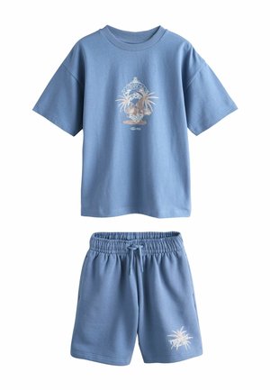 Kék rövid ujjú ing és rövidnadrág szett trópusi pálmafás grafikákkal és „Tropical” felirattal az ing elején és a rövidnadrág bal lábán.