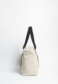 Plátěná taška v krémové barvě s černými popruhy, se zapínáním na zip v horní části, strukturálním tvarem a kontrastními bočními akcenty.