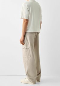 Jasnoszara bawełniana koszulka o luźnym kroju, w połączeniu z beżowymi spodniami cargo z bawełny, które posiadają boczne kieszenie. Buty są w kolorze off-white.