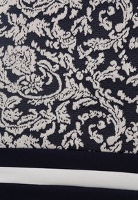 Tessuto navy con intricati motivi floreali e fogliari bianchi, su uno sfondo testurizzato e una banda orizzontale bianca in contrasto nella parte inferiore.