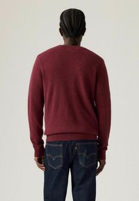 Bordeaux gebreid sweater met ribgebreide manchetten en zoom, gecombineerd met donkere denim jeans met een klassiek logopatch en stikseldetails.