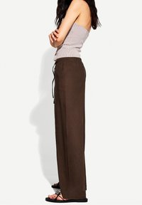 Brązowe, luźne spodnie z elastycznym paskiem w talii i sznurkiem. Lekki materiał o gładkiej teksturze. W połączeniu z paskowanym topem i sandałami.
