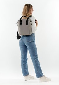 Grauer wasserdichter Rucksack mit schwarzen Griffen und Akzenten, rechteckiger Form, sichtbarem Reißverschluss und verstellbaren Schultergurten.