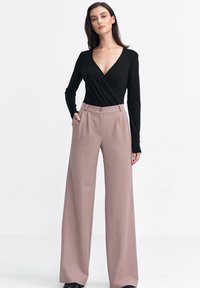 Czarna bluzka z długimi rękawami i głębokim dekoltem w kształcie litery V, zestawiona z spodniami z wysokim stanem i szerokimi nogawkami w miękkim beżowym materiale.