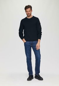Marineblauw gebreid sweater met textuurpatroon, ronde hals en zijzak, gecombineerd met blauwe jeans en zwarte schoenen. Eenvoudig, casual ontwerp.