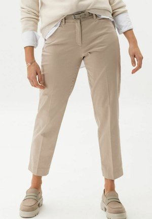 Person wearing light beige cropped pants with a belt, beige loafers, a white shirt, and a cream sweater with rolled-up sleeves.