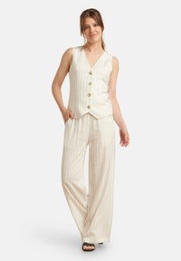 Beige-gestreifter Weste und weite Hosen mit Knopfdetails und lockerer Passform, aus leichtem Stoff gefertigt. Sandalen runden das Outfit ab.