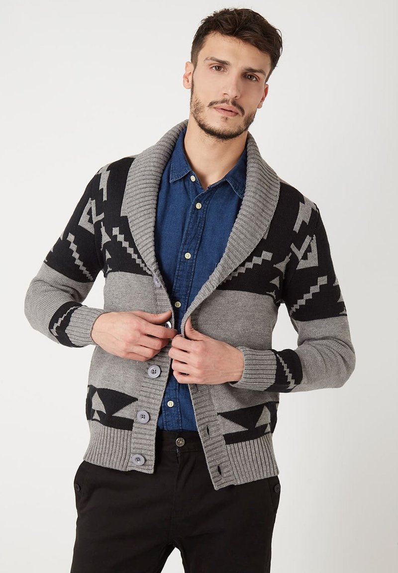 Cárdigan de punto en gris y negro con cuello de chal, patrones geométricos y tres botones, llevado sobre una camisa de mezclilla azul.