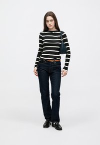 Mustvalge triibuline pika varrukaga särk, sinised teksapüksid, pruun vöö ja läikivad mustad kingad. Väike sinine käekott, minimalistlik disain.