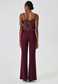 Pantalon large bordeaux avec une coupe ajustée, associé à un caraco en satin marron foncé. Les bretelles sont ajustables, ajoutant un minimum d'ornements.