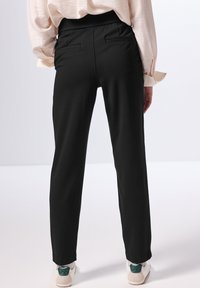 Sorte bukser med en afslappet pasform og elastisk waistband, med to baglommer og et glat, struktureret stof. Sammen med hvide sneakers.