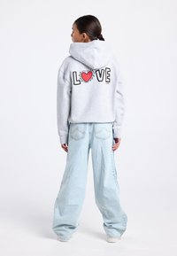 Lichtgrijze capuchontrui met het woord "LOVE" en een rood hart op de achterkant; gecombineerd met loszittende lichtblauwe spijkerbroek.