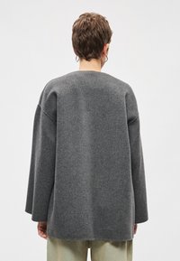 Hall hallikasüle kampsun pehme tekstuuri, ümar kaelus, langevad õlad ja pikad varrukad, lihtsa ja puhta disainiga.