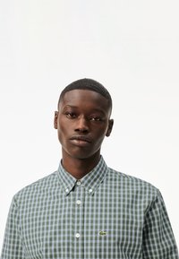Camisa a cuadros verde y azul con cuello abotonado, que presenta un pequeño logo de Lacoste. Fabricada con una tela de textura suave.