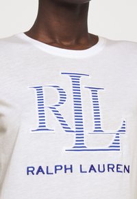 Vit bomull T-shirt med en blå broderad "RLL"-logotyp med randiga detaljer och texten "RALPH LAUREN" i blått under.