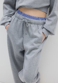Grijze sweatshirt met een cropped ontwerp en een elastische tailleband met een blauw-wit gestreepte binnenband. Getailleerde broek met zijzakken.