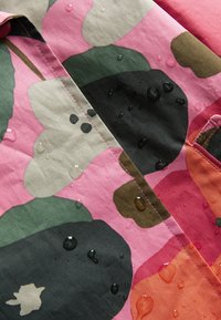 Tissu résistant à l'eau avec un motif floral en rose, vert et noir, présentant des gouttes d'eau visibles à la surface.