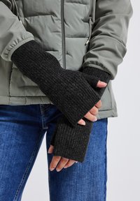 Svarta ribbade fingervantar utan fingrar gjorda av tjockt stickat material, bärs över en grå puffjacka. Vantarna har en texturerad yta och öppna fingertoppar.