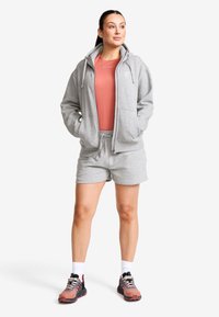 Grå zip-up hoodie med dragsko, kombinerad med en korallfärgad topp och matchande grå shorts. Har sportskor med svarta och röda accenter.