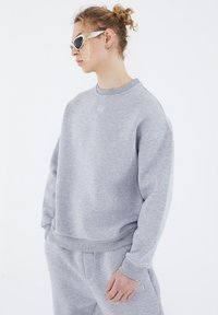 Grauer Baumwoll-Sweatshirt mit Rundhalsausschnitt, leicht oversized Passform und Rippbündchen. Besitzt ein dezentes Markenlogo auf der Brust.