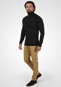 Czarny sweter typu golf wykonanego z dzianiny, dopasowany krój, zestawiony ze jasnobeżowymi spodniami i ciemnobrązowymi botkami za kostkę.