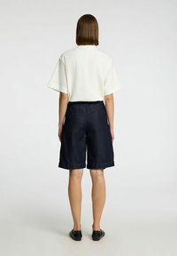 Un haut blanc à manches courtes associé à un short en denim foncé, avec une coupe décontractée et des poignets retroussés. Des ballerines noires complètent la tenue.