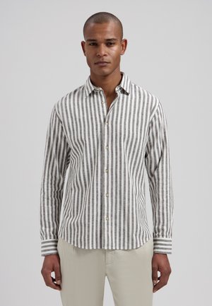 Man draagt een grijs-wit verticaal gestreept overhemd met beige broek tegen een eenvoudige lichte achtergrond.