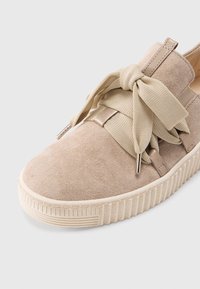 Sneaker in camoscio beige con punta arrotondata, suola spessa in gomma bianca e design con lacci in tessuto annodati in un fiocco morbido sul davanti.