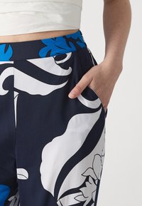 Calças florais azul-marinho com padrões brancos e azuis, apresentando uma cintura larga e bolsos laterais. Tecido suave com um ajuste descontraído.