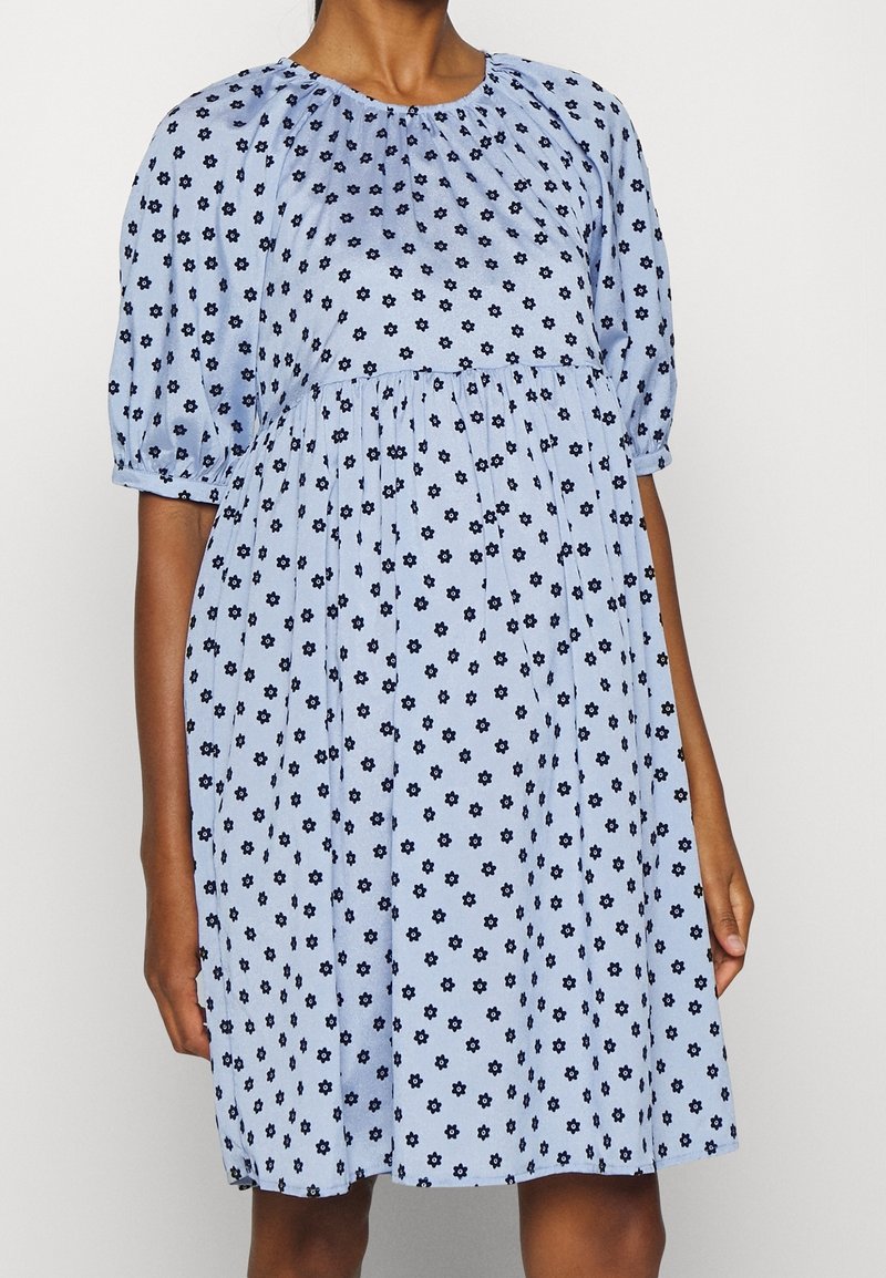 Robe bleu clair longueur genou avec motif floral noir, manches mi-longues bouffantes et encolure ainsi que taille froncées.