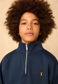 Navy blue zip-neck sweatshirt made of soft fabric, featuring a small yellow lobster embroidery on the chest and a high collar design.