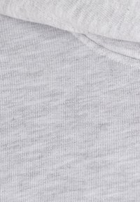 Tissu gris clair avec une surface douce et texturée, présentant un motif côtelé subtil et un bord roulé. Idéal pour une tenue décontractée.