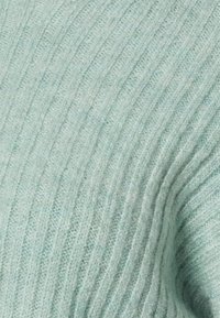 Pulôver de malha canelada verde claro com uma textura suave e variações subtis de cor do material de lã.