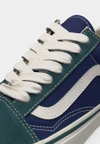 Gros plan d'une basket bleue et verte avec des lacets blancs et un détail de bande blanche ondulée sur le côté.