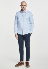 Jasnoniebieska koszula z długim rękawem zapinana na guziki, w zestawie z granatowymi spodniami slim-fit i brązowymi skórzanymi sneakersami.