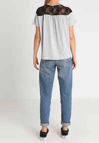 Top gris de manga corta con un encaje negro en los hombros, combinado con jeans de puño enrollado azul claro y zapatillas negras.