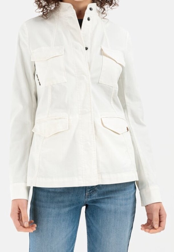 Biała kurtka użytkowa z zamkiem błyskawicznym z przodu, wysokim kołnierzem i wieloma kieszeniami. Materiał jest gładki z delikatnym połyskiem.