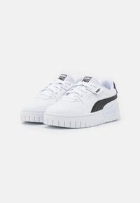Baskets blanches en matériau synthétique, avec un design texturé, une semelle épaisse blanche et un accent noir sur le côté avec le logo de la marque.