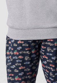 Pantaloni navy con una fantasia di piccole auto e camion d'epoca rossi, blu e bianchi, abbinati a un maglione leggero grigio.