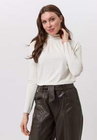 White long-sleeve turtleneck top features a gathered neckline, paired with high-waisted dark brown leather pants with a tie belt.