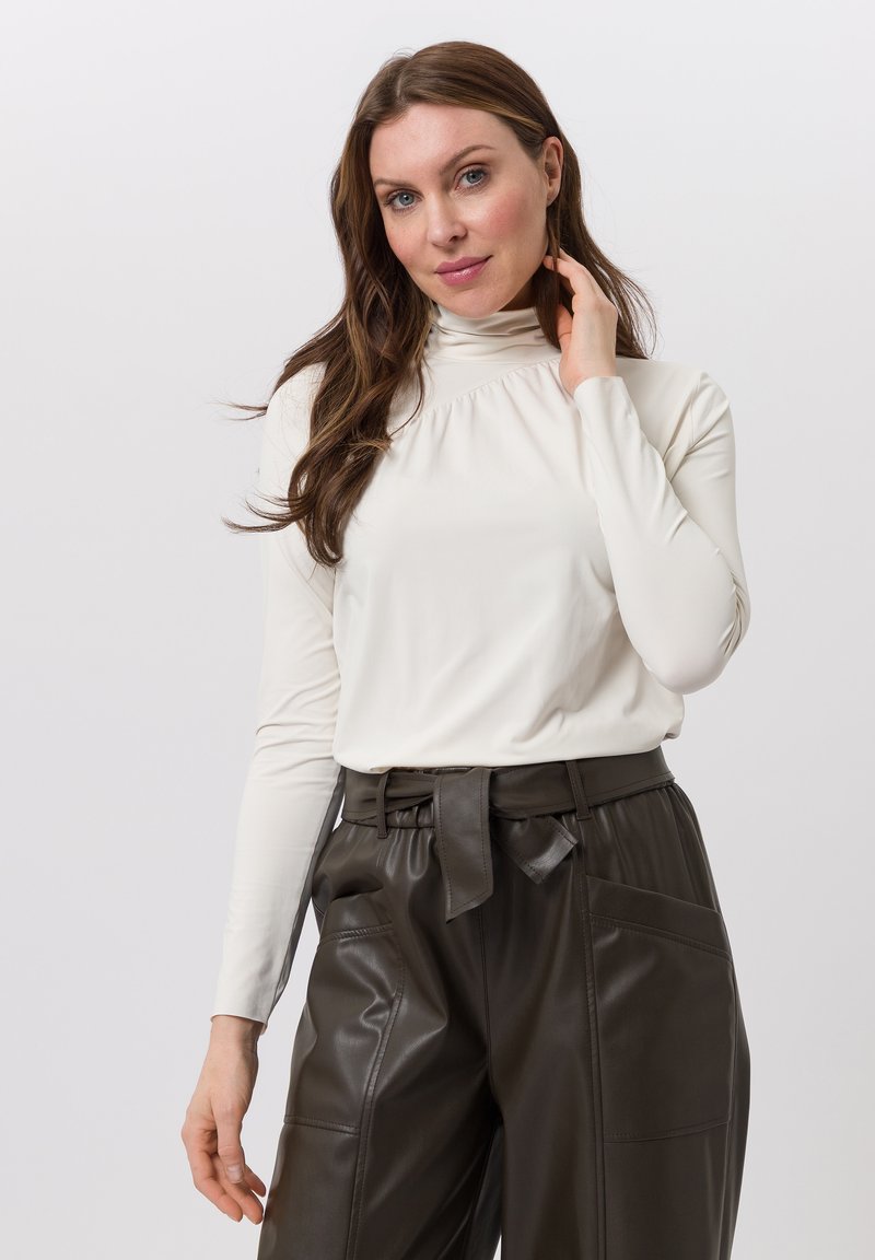 White long-sleeve turtleneck top features a gathered neckline, paired with high-waisted dark brown leather pants with a tie belt.