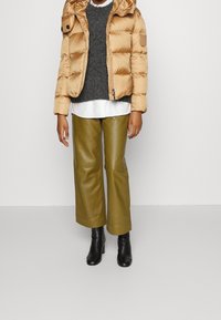 Giacca a vento beige con cappuccio, maglione grigio, camicia bianca, pantaloni larghi verde oliva e stivaletti neri. Texture lisce, hardware minimal.