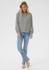 Camicia button-up a righe in bianco e nero, maniche lunghe con polsini, indossata con jeans a zampa di elefante blu chiaro e stivali alla caviglia beige.
