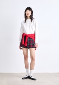 White button-up shirt, red sweater tied at the waist, navy and red plaid skirt, white ankle socks, and black Mary Jane shoes.