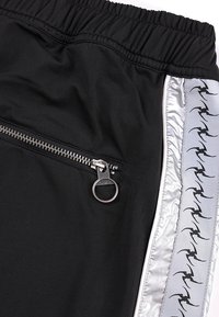 Μαύρο παντελόνι με ελαστική μέση, ασημένια τσέπη με φερμουάρ και ανοιχτό γκρι πλαϊνή ρίγα που φέρει επαναλαμβανόμενα μαύρα αφηρημένα σχέδια που μοιάζουν με πουλιά.