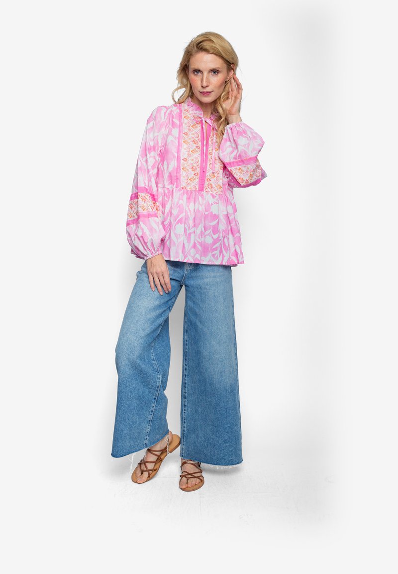 Rosa gemusterte Bluse mit Puffärmeln und geschnürtem Ausschnitt, kombiniert mit weit geschnittenen blauen Jeans und braunen Sandalen mit Riemchen.