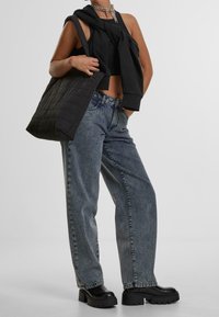 Svart ärmlös topp med knutdetalj, oversized grå jeans, svart vadderad tote-väska och chunky svarta platåskor.