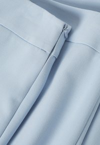 Svetle modrá tkanina s texturovaným povrchem, s diskrétním zipem podél švu. Hladký a mírně elastický materiál.