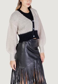 Cardigan lavorato a maglia con una combinazione di colori in contrasto tra nero e crema, caratterizzato da un design corto, tessitura strutturata e chiusura con bottoni, abbinato a una gonna frangiata in pelle nera.